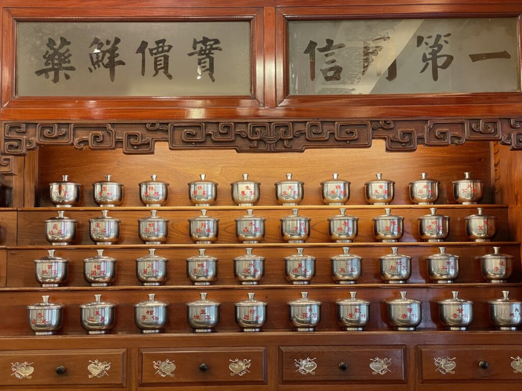 「一信第一 實價鮮藥」の扁額と陶器の生薬壺